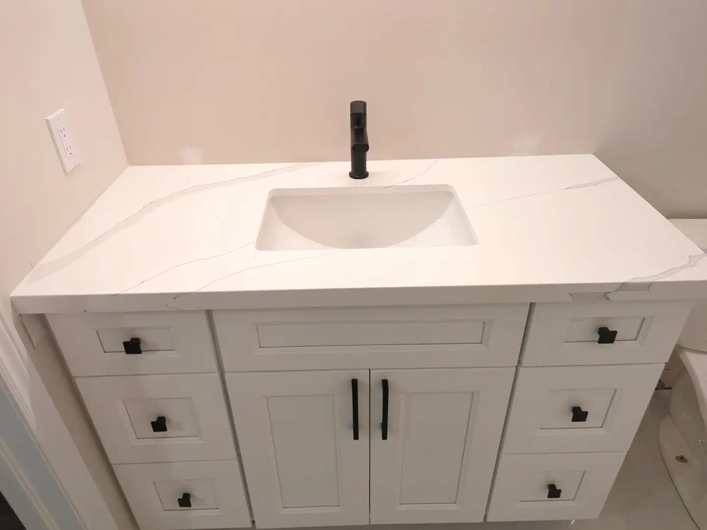 Finishing — High angle shot of a newly installed white vanity with black hardware, white quartz countertop, and black faucet.