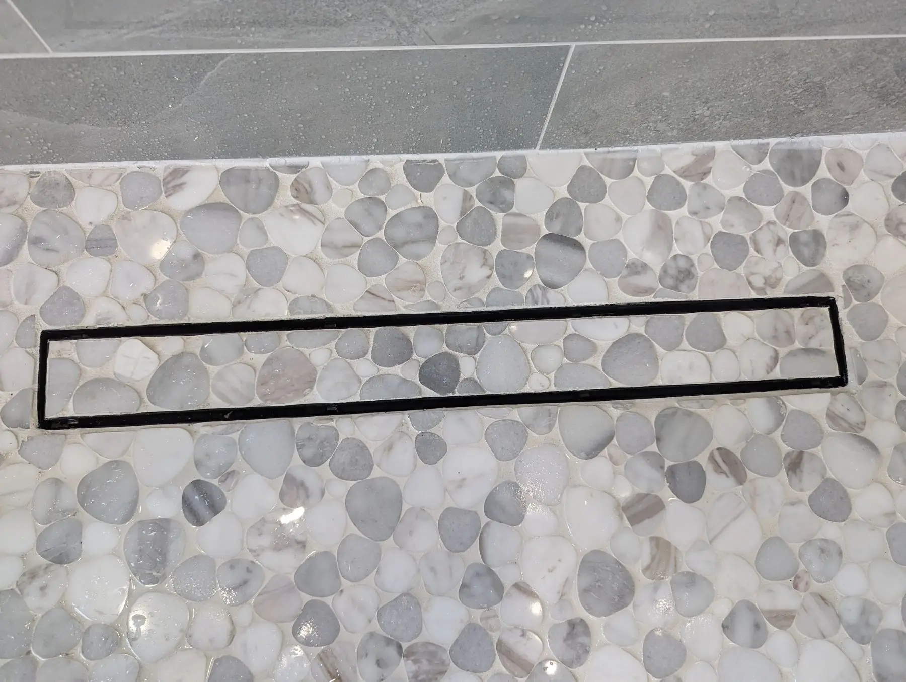 Finishing — Close-up of a linear shower drain installed within a pebble tile shower floor.
