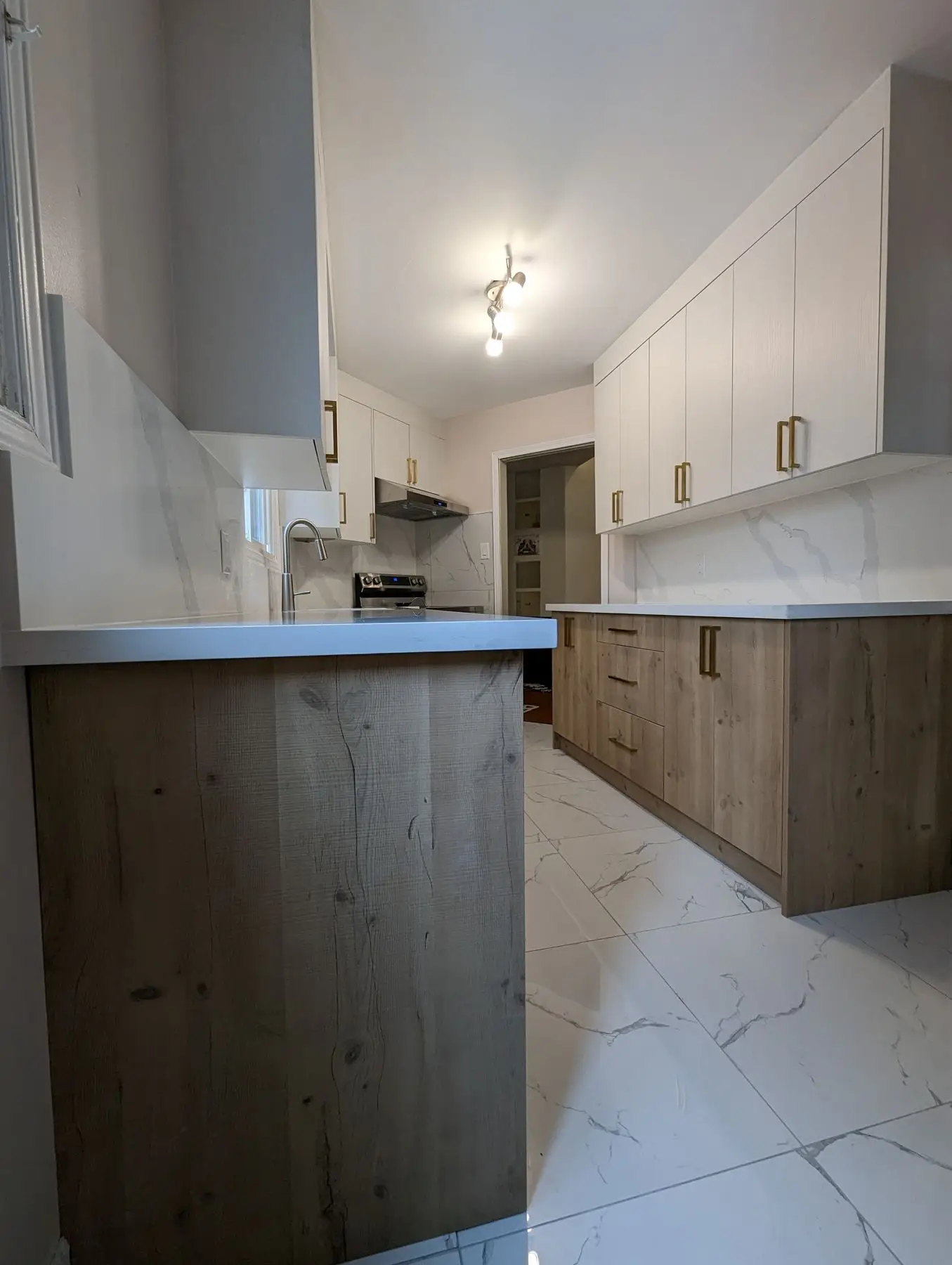 Finished — Completed modern galley kitchen with wood base cabinets, white upper cabinets, and marble-look tile flooring.