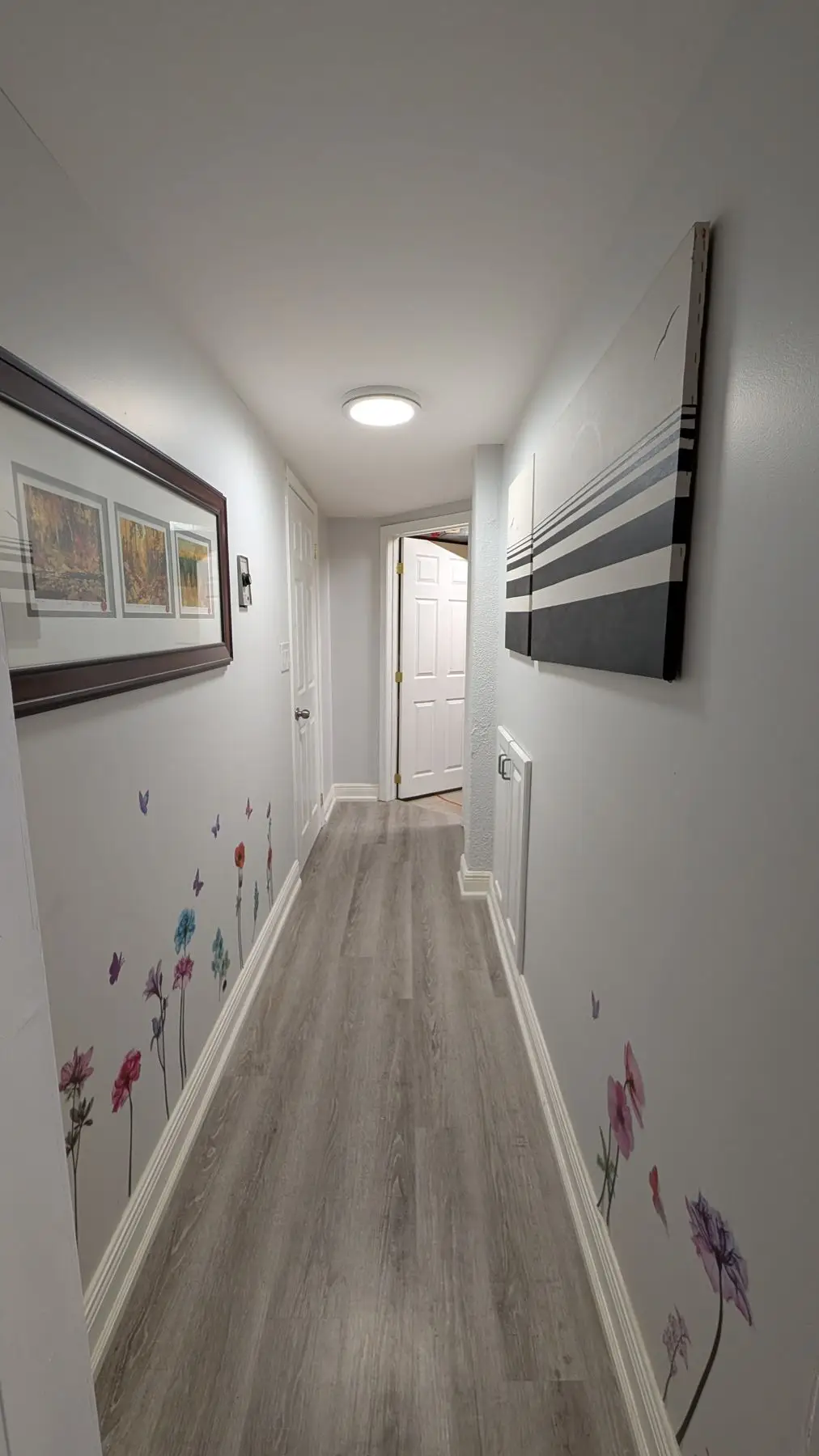 Finished — Finished hallway with grey laminate flooring, flower wall decals, and white trim.
