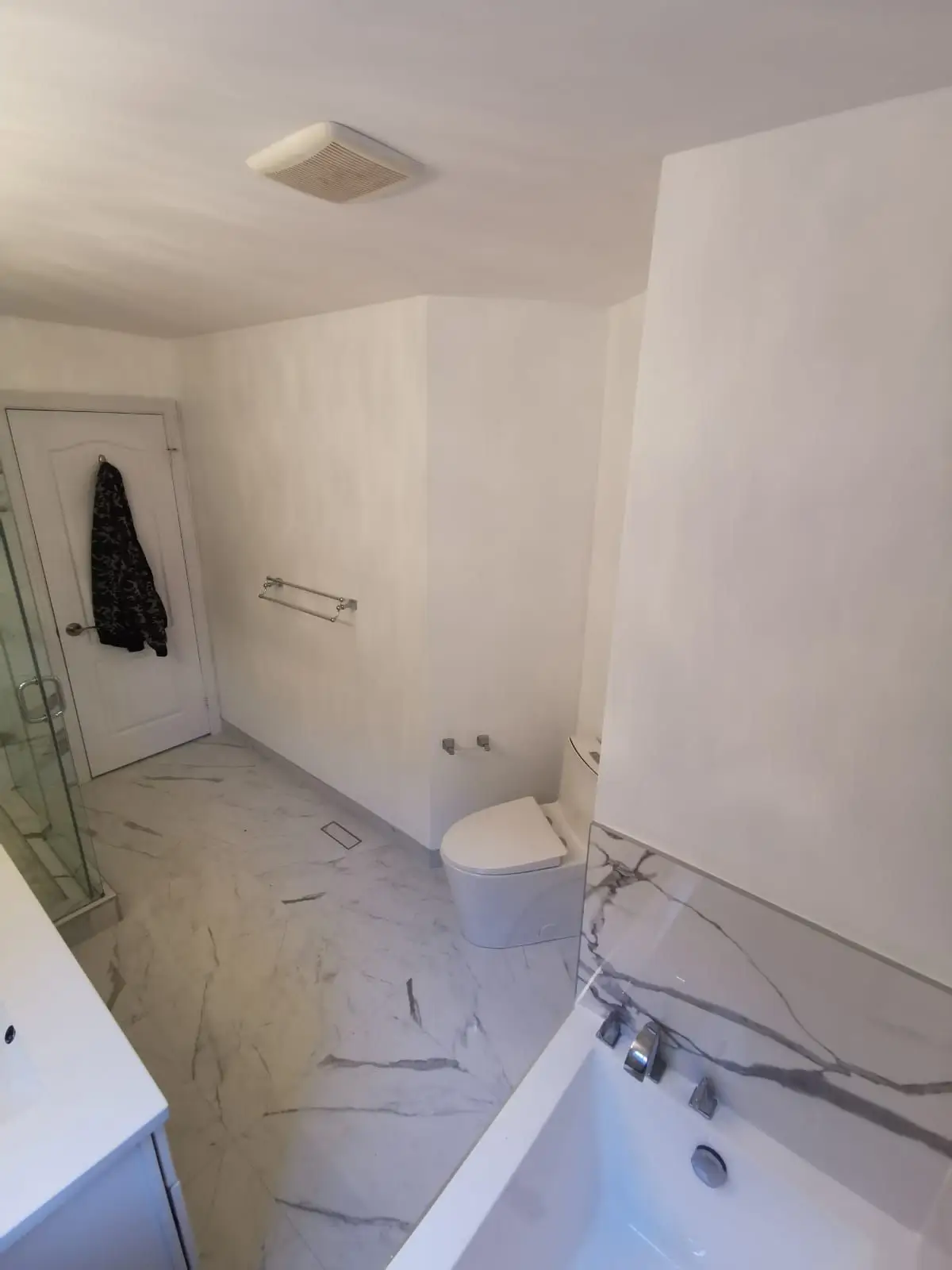 Finished — High-angle view of a finished bathroom featuring a marble tile floor, soaking tub, glass shower, and modern toilet.
