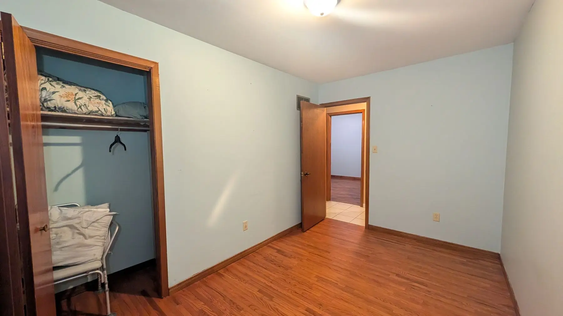 Finished — Wide shot of an empty bedroom with light blue walls, wooden closet, and hardwood flooring.