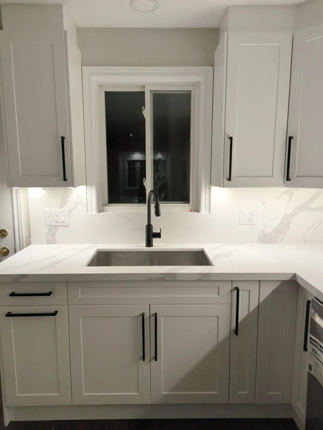 Finished — Completed kitchen sink area with white shaker cabinets, quartz countertops, and black hardware.