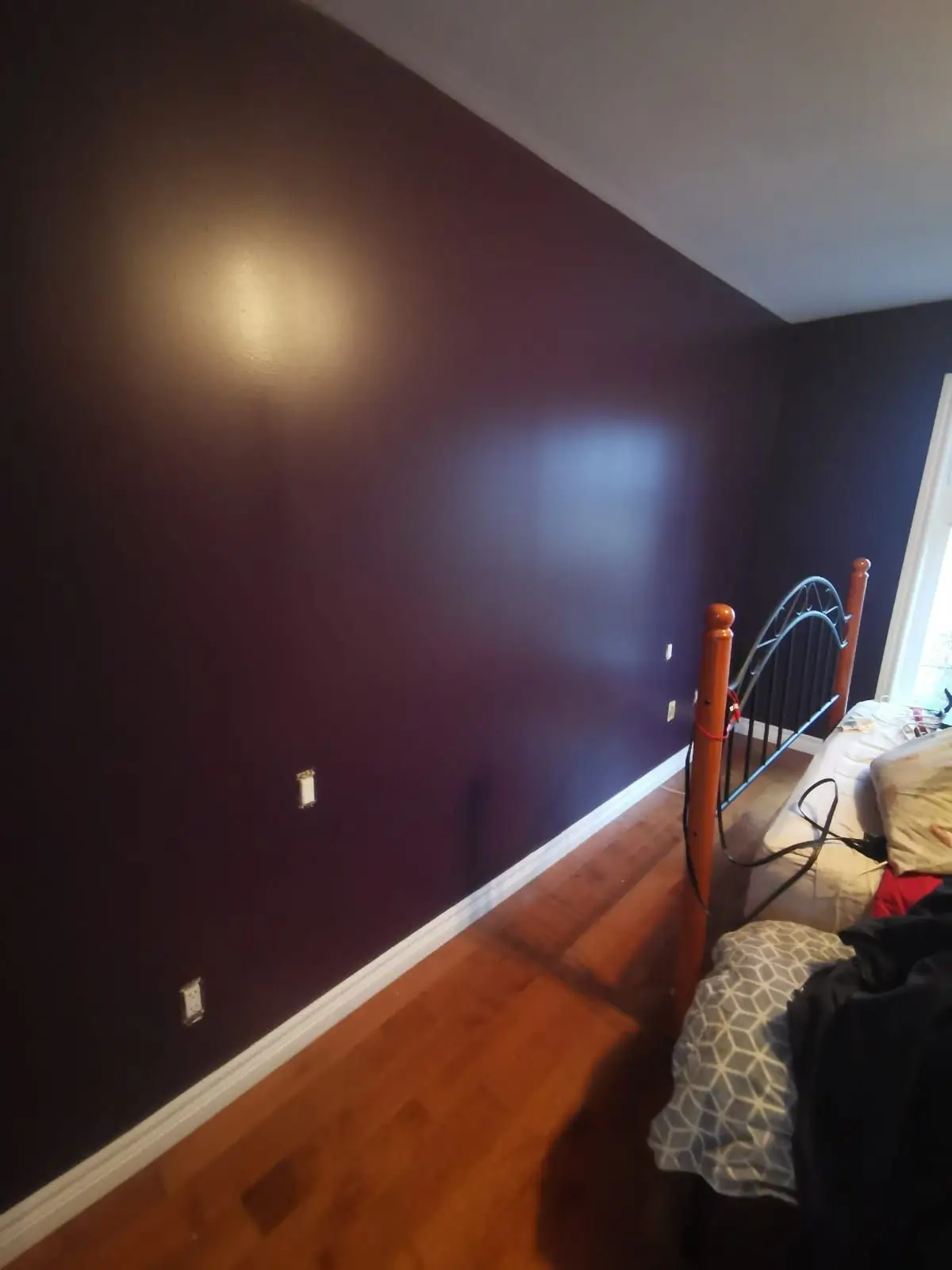 Finished — Finished bedroom featuring dark purple walls, hardwood flooring, and white baseboards with a bed partially visible.