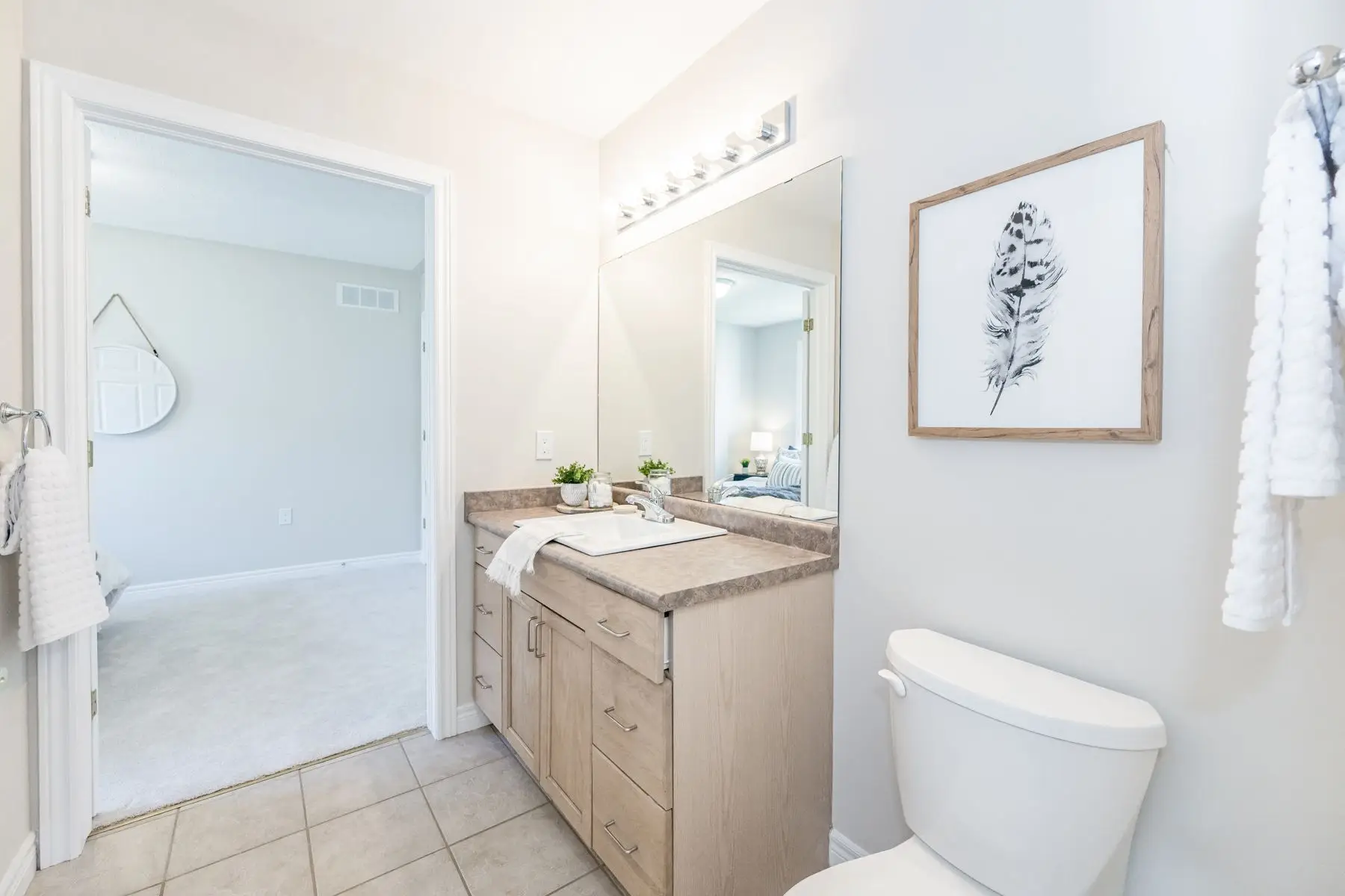 Finished — Completed bathroom featuring wooden vanity, large mirror, and white toilet with doorway view into adjacent bedroom.