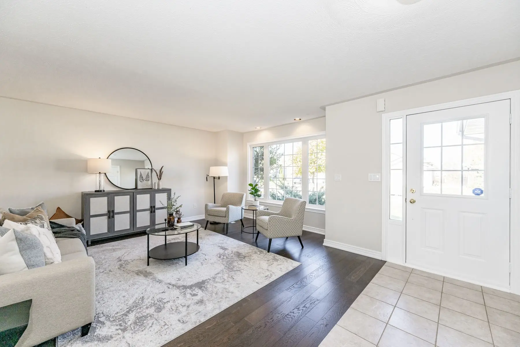 Finished — Completed bright living room with dark hardwood floors, white entry door, and staged furniture.